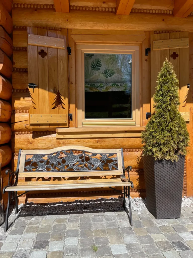 dom z bali, okno z okiennicami, ławka przed domkiem, tuja w donicy